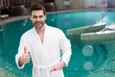 başparmak gösterilmesini ve spa merkezi kamerada gülümseyen bornoz yakışıklı genç adam