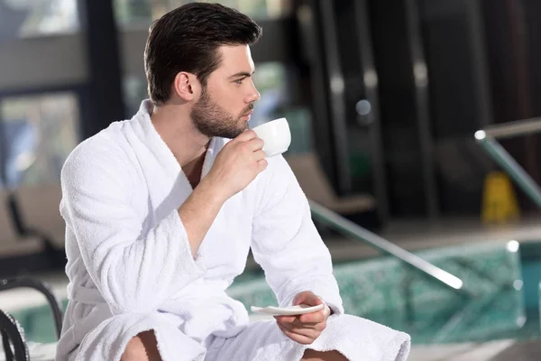 Handsome Young Man Bathrobe Drinking Coffee Looking Away Spa Center — Stock Photo, Image