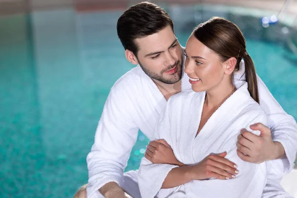 Feliz Pareja Joven Albornoces Abrazando Cerca Piscina Centro Spa —  Fotos de Stock