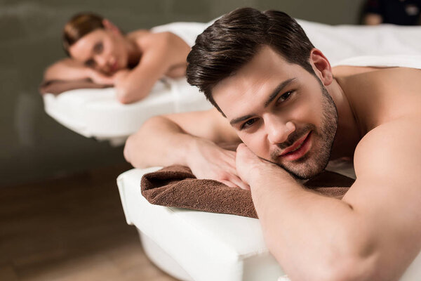 handsome young man looking at camera while having massage in spa salon 