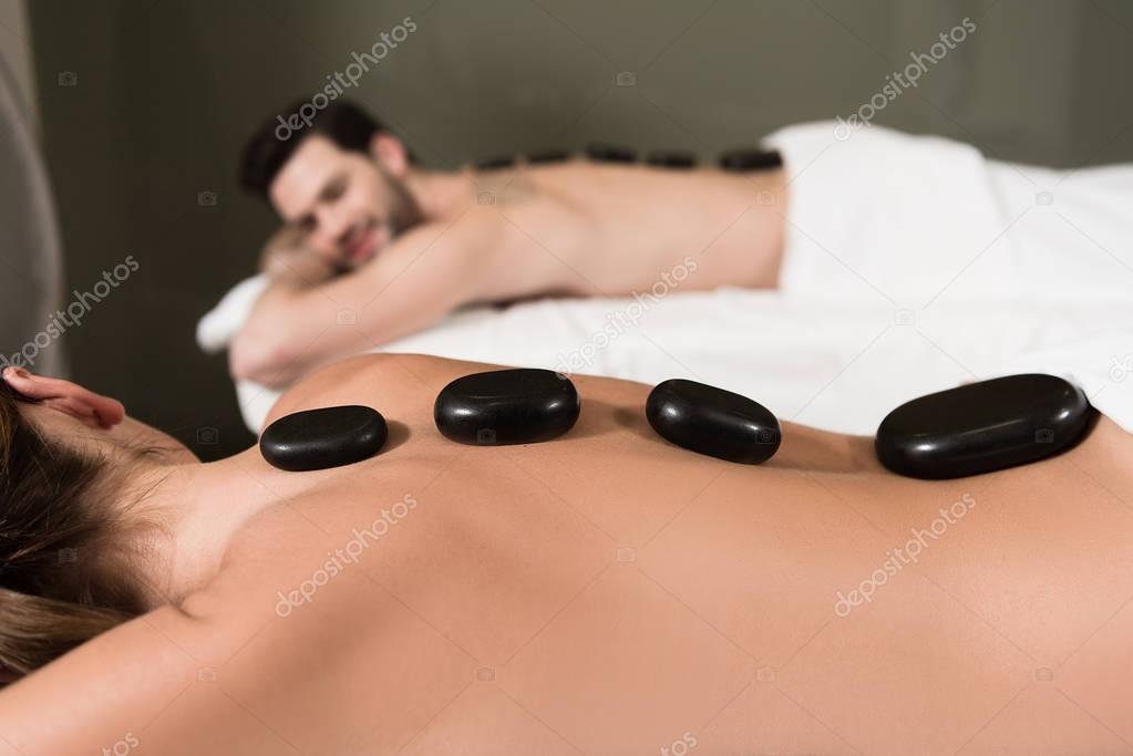cropped shot of couple looking at each other while having hot stones massage in spa center 
