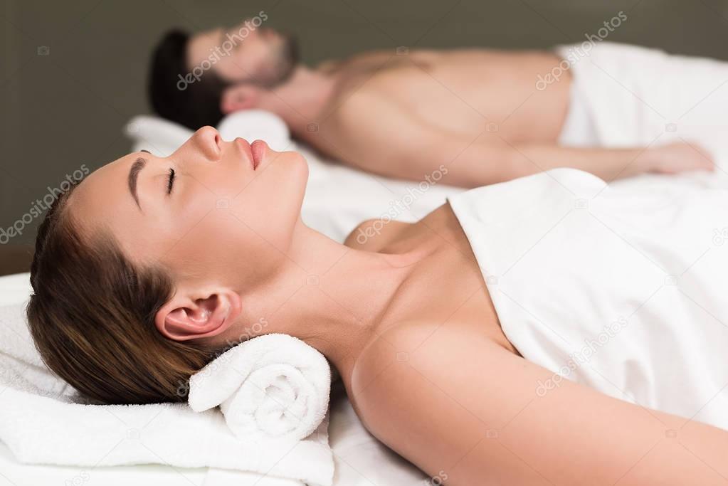 side view of couple with closed eyes lying in spa center