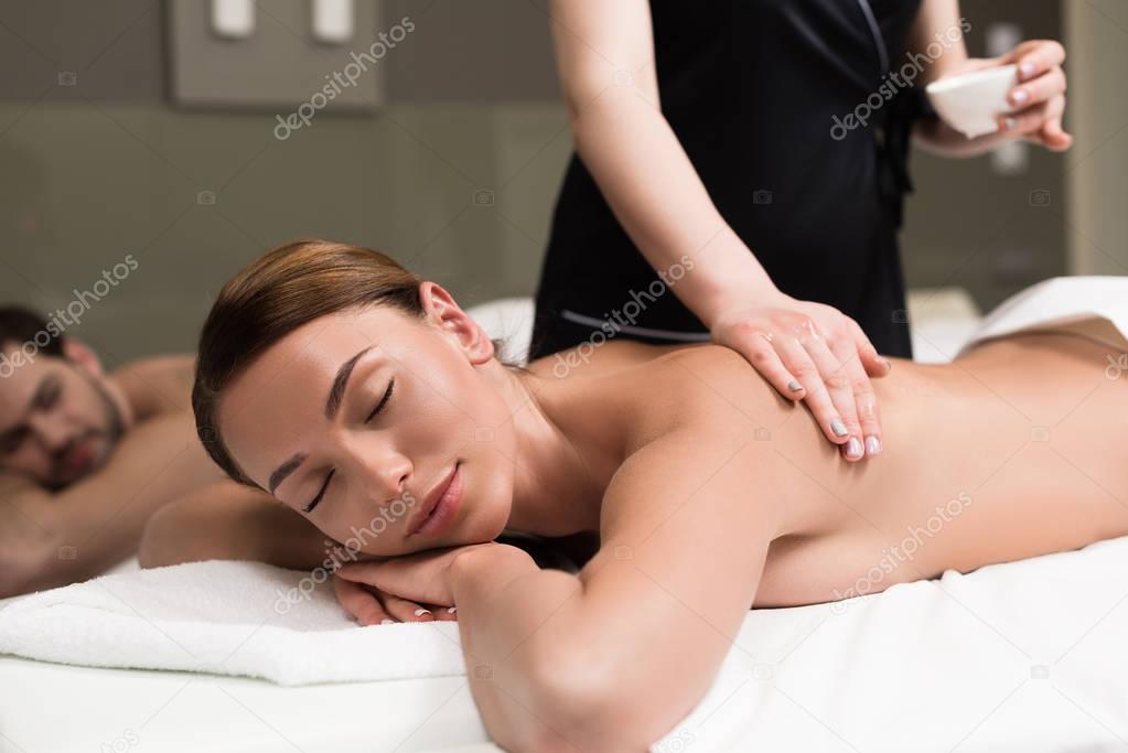 young woman with closed eyes having body massage in spa salon
