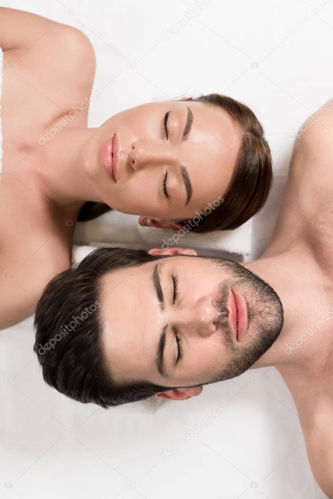 top view of beautiful couple with closed eyes lying together in spa center