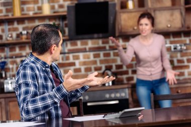 selective focus of wife and husband having argument in kitchen at home, financial problems concept clipart