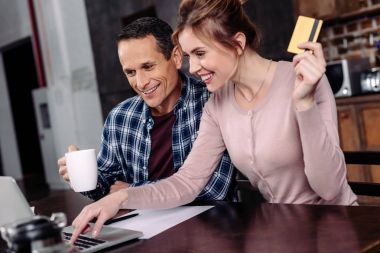 kredi kartı ve evde dizüstü bilgisayar ekranına bakarak kahve ile mutlu çift