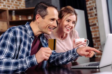 kredi kartı ve evde dizüstü bilgisayar ekranına bakarak kahve ile mutlu çift