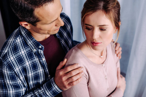 side view of man hugging upset wife at home