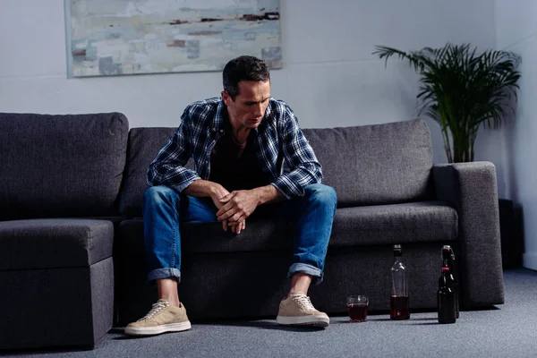 man looking at alcohol on floor while sitting on sofa at home