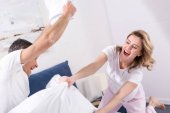 happy couple having pillow fight in bedroom at home