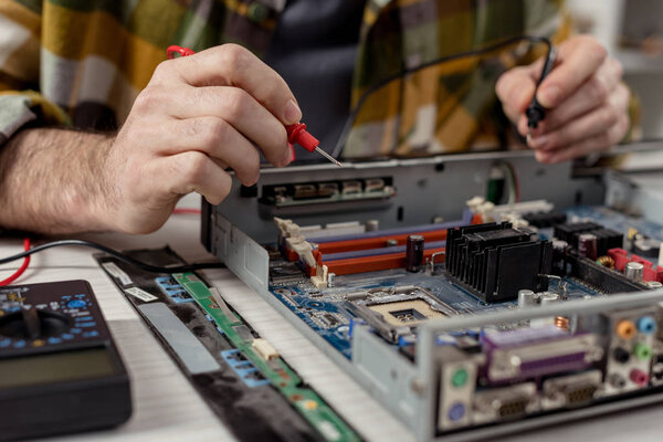 обрезанное изображение рук с мультиметром и сломанным компьютером
 