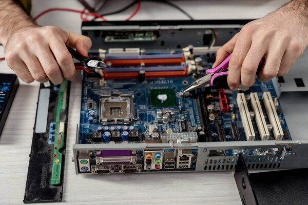 cropped image of hands with tongs fixing motherboard of pc 