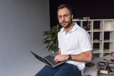 masada oturan ve dizüstü bilgisayar kullanarak bir adam 