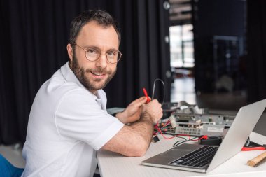 adam kameraya multimetre elinde tutarken bakan gülümseyen