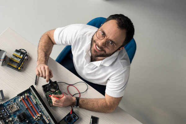 overhead view of smiling man holding multimeter and magnifier in hands