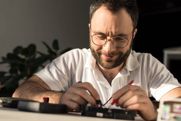 smiling man using multimeter while fixing pc