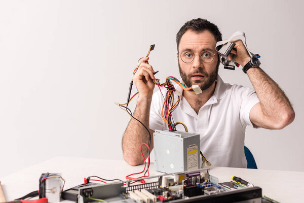 bewildered man holding wires and computer parts in hands  