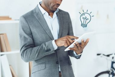 Afrika kökenli Amerikalı adam ampul simgesi ile dijital tablet kullanarak görüntü kırpılmış