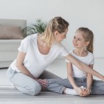 Mother teaching daughter how to sit in yoga butterfly pose