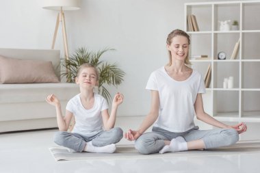 Anne ve kızı lotus poz evde oturan ve birlikte meditasyon