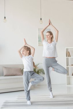 beautiful mother and daughter balancing in tree pose together clipart