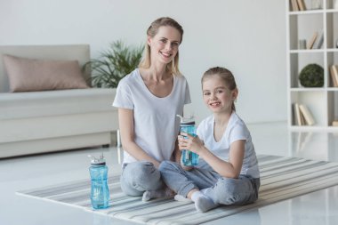Anne ve kızı ile fitness su şişeleri yoga paspaslar üzerine oturan