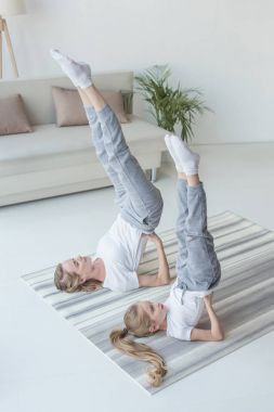 mother and daughter practicing yoga in Supported Shoulder Stand pose at home clipart