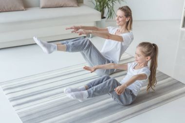 mother and daughter doing v-sit crunches on yoga mat