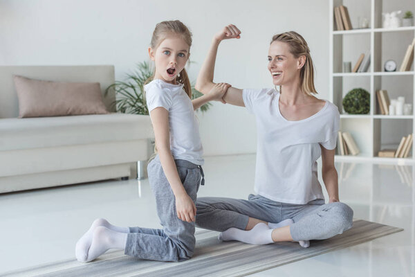 мать показывает бицепсы мышцы своей потрясенной дочери дома
