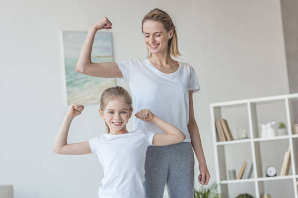 happy fit mother and daughter showing biceps muscles