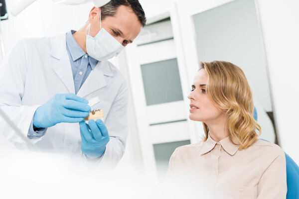 Doctor showing jaws model to female patient in modern dental clinic