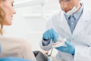 Modern diş kliniğinde kadın hastaya çene modeli gösteren doktor