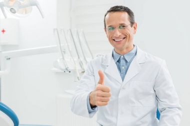 Modern diş kliniğinde dişçi baş parmağını gösteriyor.