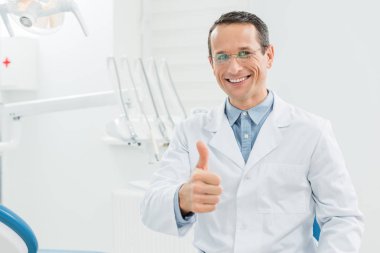 Dentist showing thumb up in modern dental clinic clipart