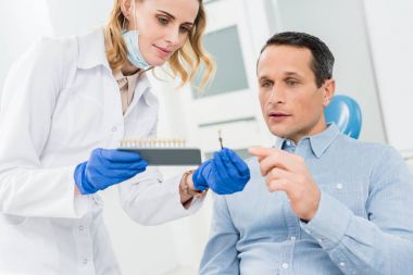 Modern diş kliniğinde diş implantlarını seçen kadın doktor ve hasta.