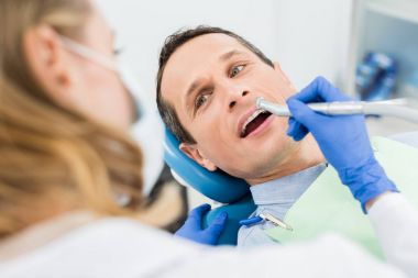 Modern diş kliniğinde dişçi matkabı kullanan erkek hasta