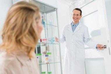 Smiling doctor welcoming female patient in modern dental clinic clipart