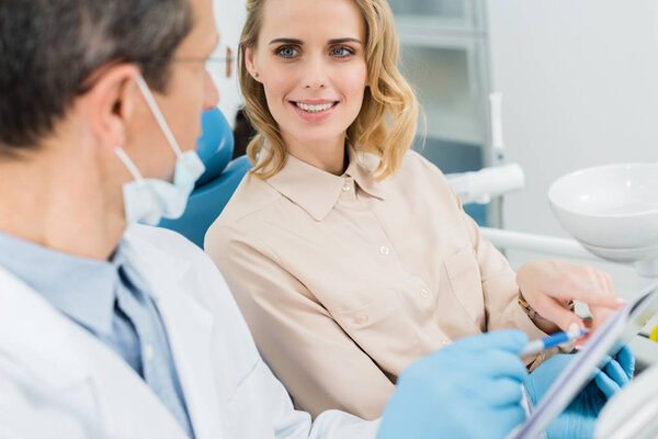 Woman consulting with dentist looking at clipboard in modern clinic