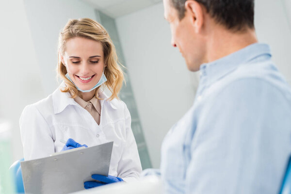 Patient and smiling doctor recording diagnosis in modern dental clinic