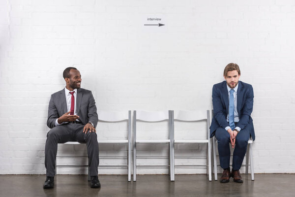 smiling african american businessman looking at scared colleague while waiting for job interview