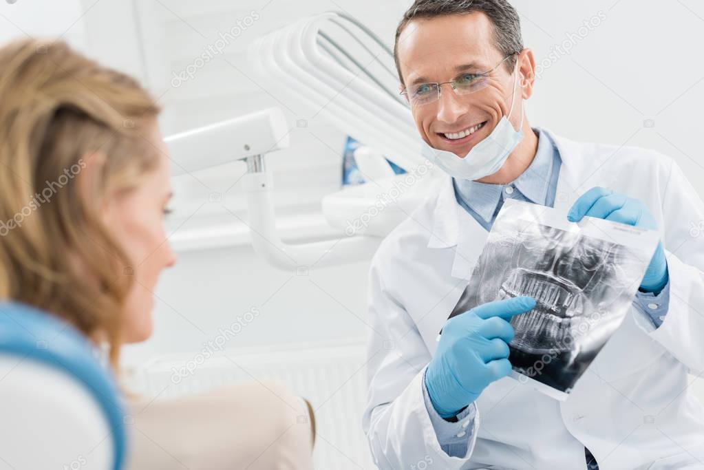 Male dentist showing female patient x-ray in modern dental clinic
