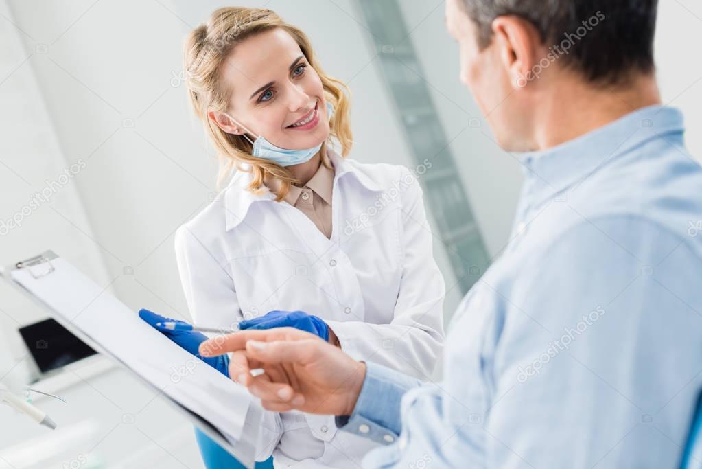 Man consulting with female dentist recording diagnosis in modern clinic
