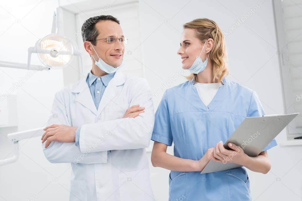 Smiling confident doctors looking at each other in modern dental clinic