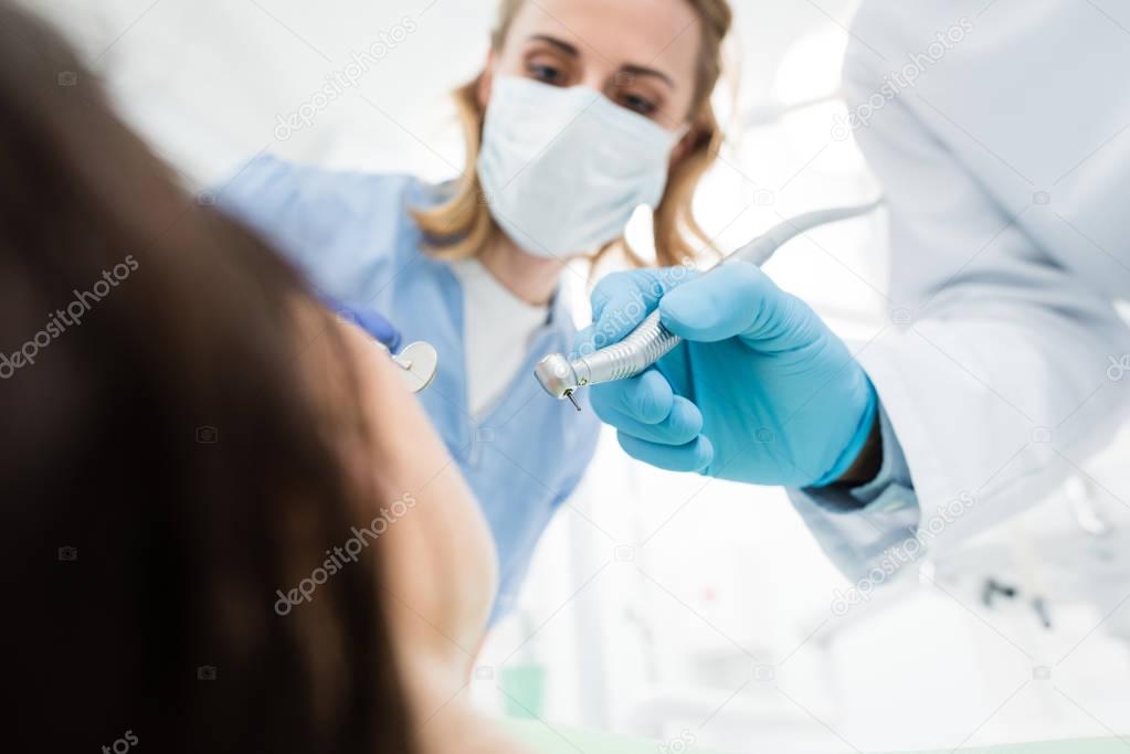 Doctors using dental drill during procedure in modern dental clinic