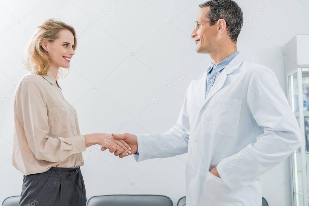 Male doctor and female patient shaking hands in modern dental clinic