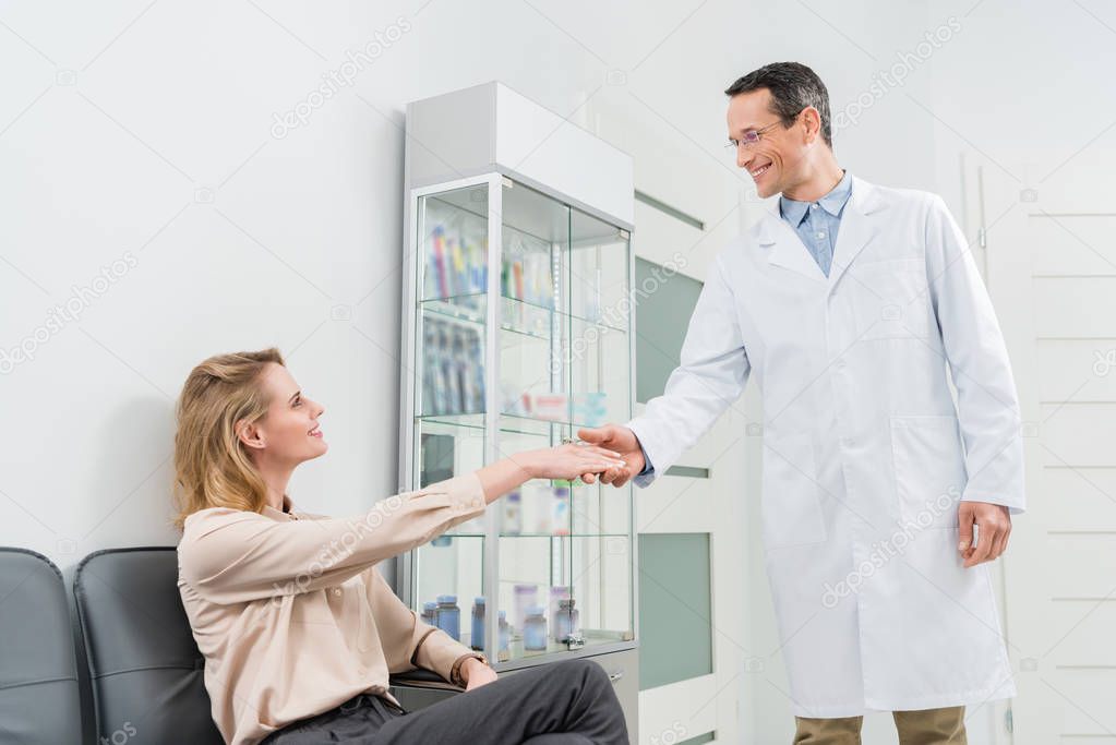 Smiling doctor greeting female patient shaking hands in modern dental clinic