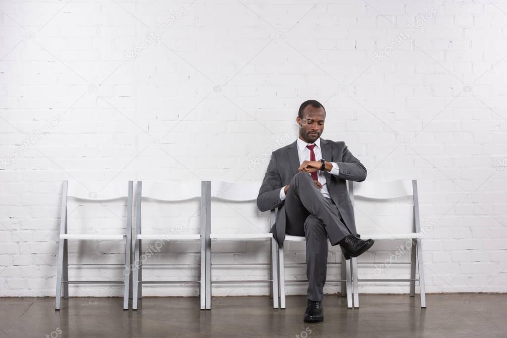 african american businessman checking time while waiting for job interview