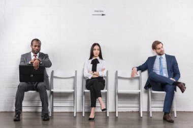 multiethnic young business people sitting on chairs while waiting for job interview clipart
