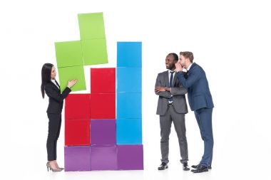 multicultural businessmen looking at asian businesswoman collecting colorful blocks isolated on white clipart