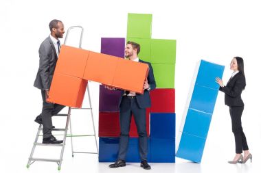 multiethnic business colleagues collecting colorful blocks isolated on white, business cooperation concept clipart